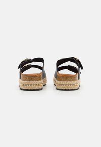 Black sandals featuring a textured sole, two wide straps, and a natural-colored espadrille platform with a decorative bead accent.