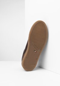 Sole di scarpa in pelle marrone con suola in gomma testurizzata, completa di logo e dettagli sulla taglia, inclinata su uno sfondo chiaro.