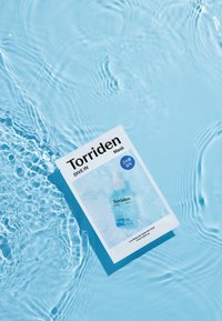 Torriden Dive In Maskin vaalea sininen tausta, jossa on vesipisaroiden kuvio ja teksti paksulla mustalla fontilla, kiiltävässä paperissa.