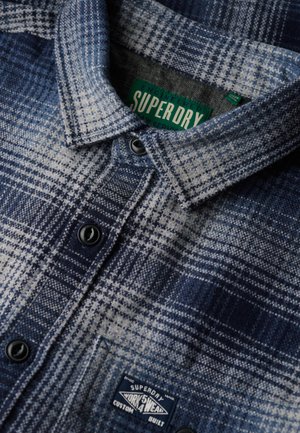 Blauw en wit geruit flanellen overhemd met een button-down kraag, zwarte knopen en een merkpatch op de zak.