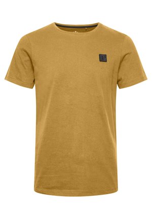 Tričko s krátkym rukávom v horčicovo žltej bavlnenej farbe, s kruhovým výstrihom a malou čiernou štvorcovou nášivkou na ľavej strane hrude.