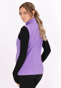 Gilet in pile viola con colletto alto, caratterizzato da una superficie liscia. Indossato sopra un top nero a maniche lunghe, mostra linee di design continue.