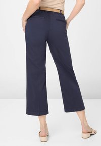 Marineblaue weite Hosen mit glatter Textur, ausgestattet mit einem dehnbaren Bund und Gesäßtaschen. Kombiniert mit beigen Sandalen mit offener Zehenpartie.