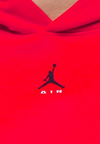 Silhouette noire d'un joueur de basketball sautant avec un ballon, au-dessus du mot « AIR », sur un tissu rouge.