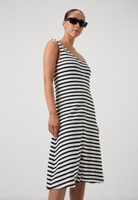 Robe rayée noir et blanc en tissu côtelé, avec un décolleté en V, des boutons sur le devant et des bretelles ajustables.