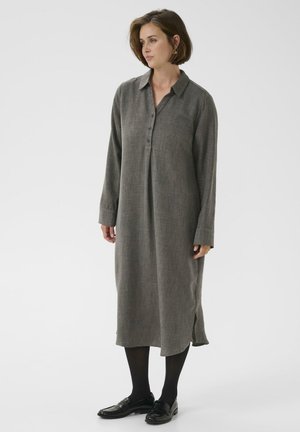 Grijze langwerpige button-up jurk met lange mouwen, gemaakt van textuurstof, met een kraag, zijsplitten en een ontspannen fit, gecombineerd met zwarte schoenen en maillots.