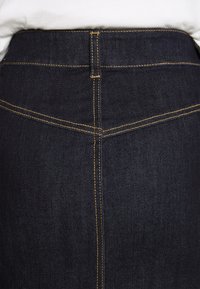 Tmavě modrá džínsová sukně s vysokým pasem, žlutým prošitím a hladkým povrchem. Obsahuje zadní kapsy a úzký střih.