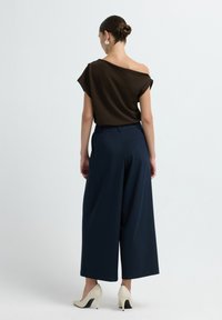 Top marrone con spalle scoperte abbinato a pantaloni a gamba larga blu navy e scarpe con tacco cremoso. L'outfit presenta una vestibilità rilassata e una texture morbida.