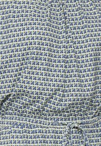 Blau-grün gemusteter Stoff mit geometrischen Formen, elastischem Bund und Kordelzugdetail. Glatte Textur.