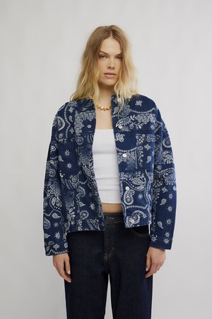 Denim jacket with blue and white paisley pattern, featuring a collar, button front, and two patch pockets. Worn over a white top.