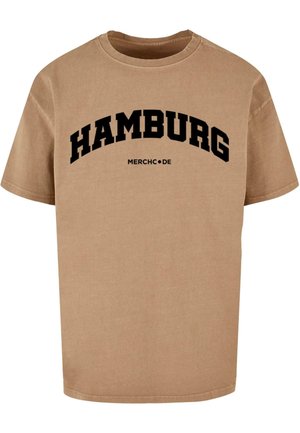 Beige bomulds t-shirt med sort tekst der læser "HAMBURG" i et buet design over "MERCHC.DE." Kortærmet og med rund hals.