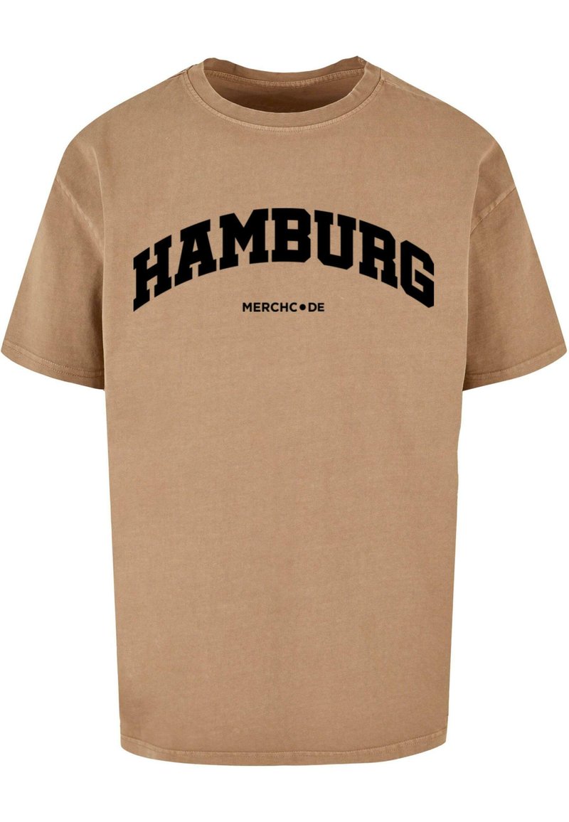 Beige bomull T-skjorte med svart tekst som sier "HAMBURG" i en buet design over "MERCHC.DE." Korte ermer og rund hals.