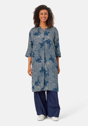 Tunique bleu marine avec des motifs floraux et à rayures, manches 3/4 et col ; associée à un pantalon en denim à jambes larges et des baskets blanches.