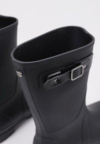Bottes de pluie en caoutchouc noir avec une texture lisse, dotées d'un détail de boucle sur le côté et d'une bordure supérieure arrondie. Convient pour les conditions humides.