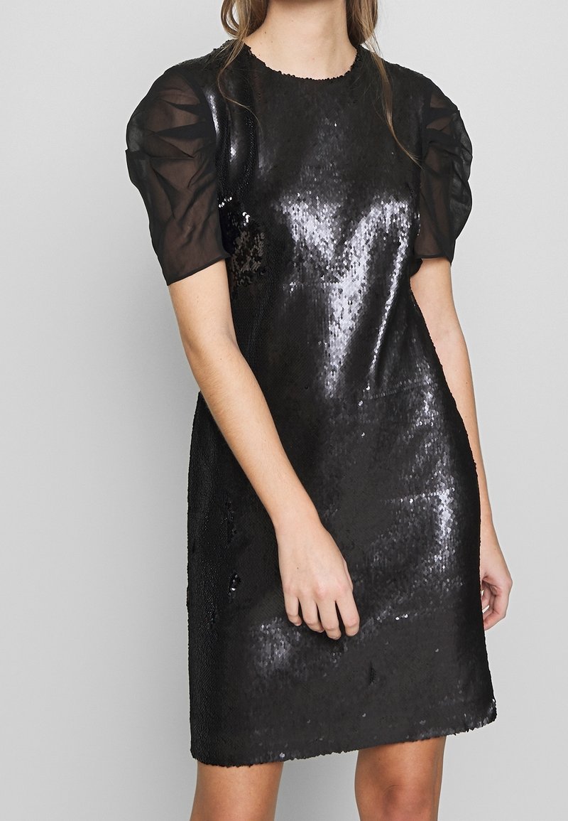 Černé šaty s flitry a nabíranými průhlednými černými rukávy a kulatým výstřihem. Hladká textura s přiléhavým stylem, design do délky kolen.