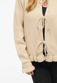Strikket beige cardigan med løs passform, med knyting ved halsen, ribbet kant og utsvingede ermer. Myk tekstur.