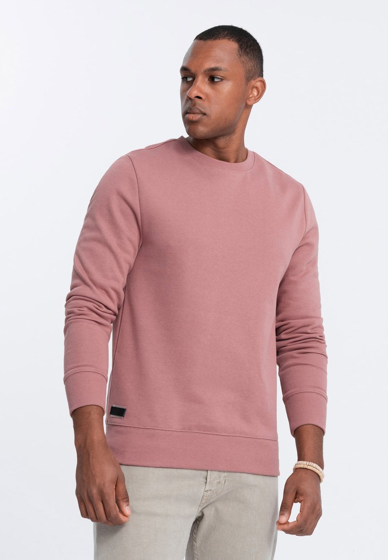 Felpa rosa realizzata in morbido tessuto, con scollo rotondo, maniche lunghe, polsini a costine e una piccola etichetta con logo all'orlo.