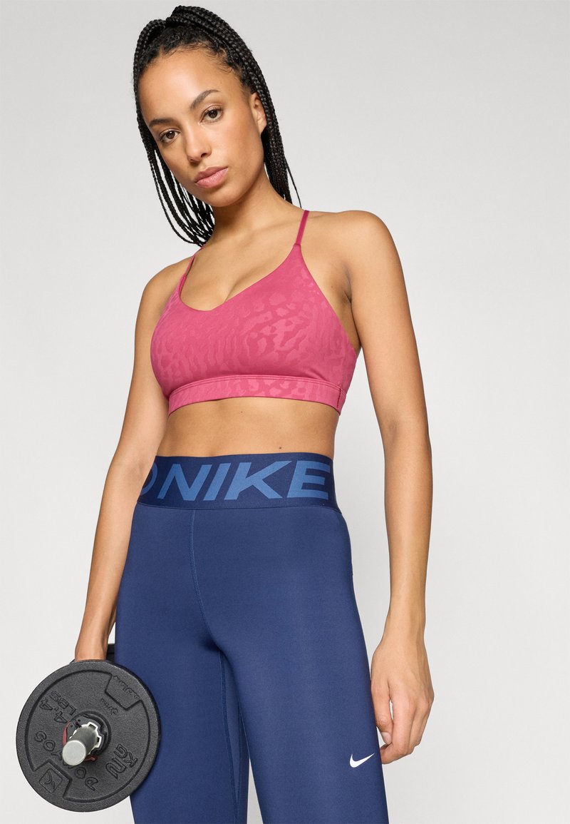 Sport bra in dark pink with a subtle animal print, paired with navy blue leggings featuring a wide logo waistband. Weights in hand.
