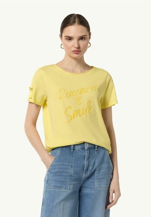 Gelbes Baumwoll-T-Shirt mit dem Text "Denk daran zu lächeln" in einem leicht dunkleren Gelb. Kurze Ärmel mit gerafftem Detail an den Bündchen.