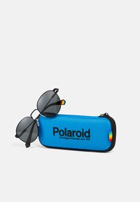 Mustad mustade polariseeritud päikeseprillidega, millel on ümmargused läätsed, puhkas sinisel kõval karbil, millel on Polaroidi logo ja mitmevärviline aktsenttriip.