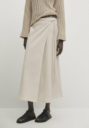 Beige polven mittainen kietaisuhame sivusolmulla, kevytkangasta. Yhdistetty mustiin remmikenkiin, jotka paljastavat avoimet varpaat.