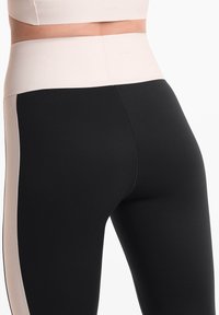 Fekete leggings magas derékkal, krémszínű oldalsó panellel és puha textúrával. Finom varrási részletek és márkalogó is található rajta.