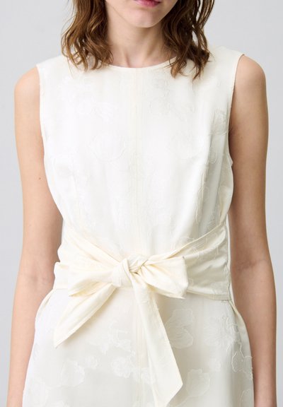 Vestido blanco sin mangas con un patrón floral en relieve, que presenta un lazo en la cintura y una textura suave y ligeramente brillante.