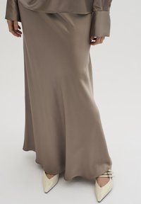 Lang, taupe satin nederdel med en glat overflade, flydende design og subtil glans, parret med spidse elfenbenhæle med accenthardware.