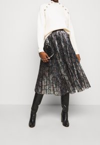Falda plisada hasta la rodilla con un brillo metálico y detalles coloridos, combinada con un suéter blanco texturizado y botas negras hasta la rodilla.