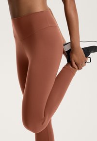 Pantalone legging s visokim strukom, prilagođeni tijelu, u tamno narančastoj boji; izrađeni od rastezljivog materijala s glatkom teksturom i bez vidljivih uzoraka ili hardverskih dodataka.