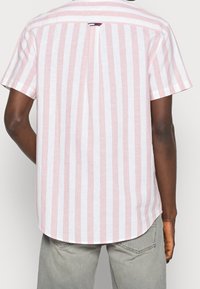 Camicetta a maniche corte con righe verticali rosa e bianche, con una piega sul retro e un orlo arcuato. Il materiale sembra leggero e traspirante.