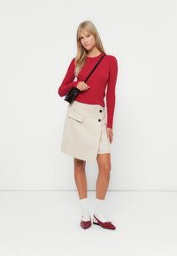 Rød, ribbete langermet topp kombinert med en beige omslagskjørt med en frontlomme og to svarte knapper, komplementert med røde sko og hvite sokker.