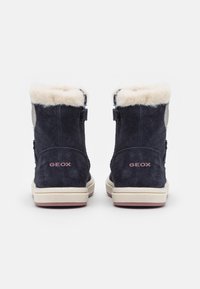 Námořnické semišové kotníkové boty s umělou kožešinou na límci, béžové gumové podrážky a růžové logo GEOX na patě. Obsahují nastavitelné popruhy po stranách.