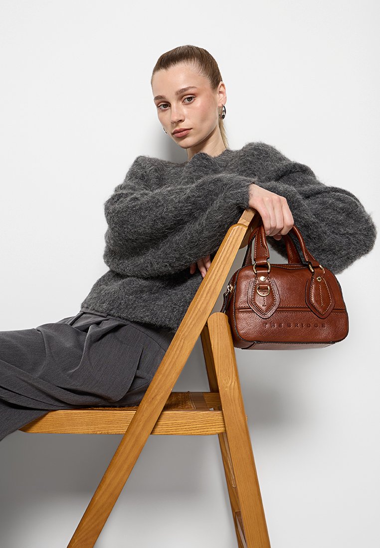 Braune Lederhandtasche mit strukturierter Oberfläche, doppelten Griffen und geprägten Details, kombiniert mit einem gemütlichen grauen Sweater und lockeren grauen Hosen.