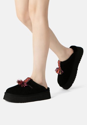 Black suede slip-on shoes with a textured tread, featuring a colorful tassel and patterned accent at the opening.