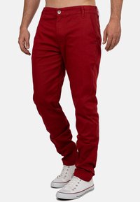 Pantaloni rossi in cotone con vestibilità slim, dotati di chiusura con bottone frontale e tasche laterali. Abbinati a sneakers bianche.