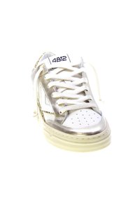 Sneaker bianco con accenti metallici argento, dettagli perforati, lacci piatti e suola in gomma testurizzata. Marchio visibile sulla linguetta.