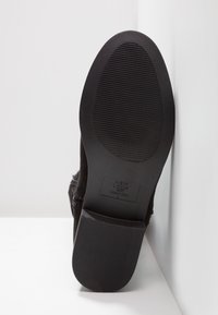 Semelle d'une chaussure noire avec une semelle texturée antidérapante et un talon bloc, affichant la marque "New Look" et le texte "Made in China" au bas.