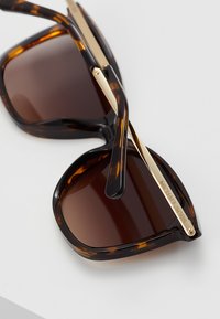 Tortoiseshell sunglasses with brown lenses, featuring gold metal accents on the arms, and a glossy finish. Marked with "MICHAEL KORS".
