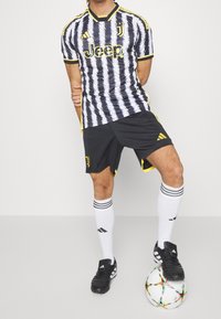 Juventusin jalkapallovaruste, johon kuuluu mustavalkoinen raidallinen paita, mustat shortsit keltaisilla yksityiskohdilla, valkoiset sukat ja mustat jalkapallosukat.