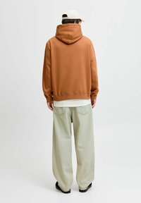 Brun huvtröja med en avslappnad passform, kombinerad med ljusgröna vida jeans. Outfits kompletteras av en ljusfärgad keps.
