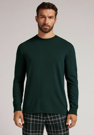 Chemise à manches longues vert foncé en tissu doux, avec un col rond et des poignets ajustés, associée à un pantalon de pyjama à carreaux.