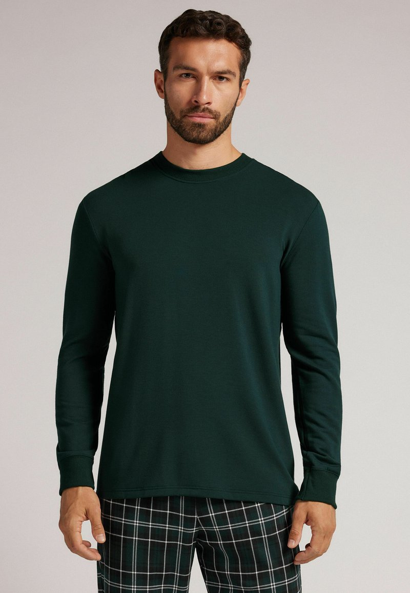 Ciemnozielona koszula z długim rękawem, wykonana z miękkiego materiału, z okrągłym dekoltem i dopasowanymi mankietami, zestawiona z piżamowymi spodniami w kratkę.