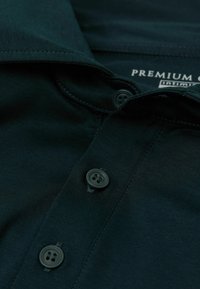 Schwarzes Polohemd mit Kragen, zwei Knopfverschluss, weicher Textur und genähten Details am Kragen.