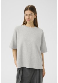 T-shirt grigio oversize con maniche corte, girocollo e una texture morbida. Abbinato a pantaloni beige scuri sartoriali.