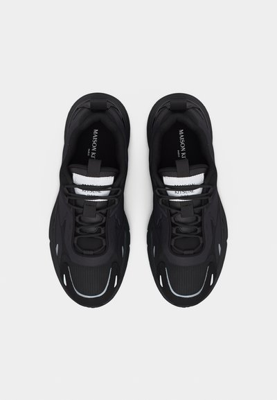 Paire de baskets noires Maison Kitsuné avec semelles épaisses, détails en mesh et étiquettes de logo blanches sur la languette, vues de dessus sur fond blanc.