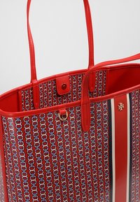 Czerwona torba na ramię w wzory z gładkimi skórzanymi uchwytami, z złotym wykończeniem, wewnętrzną kieszenią i odważnym wzorem w paski.