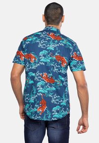 Camisa de manga corta en color azul marino con estampado de tigres naranjas y follaje verde. Presenta un cuello con solapa y un dobladillo recto.