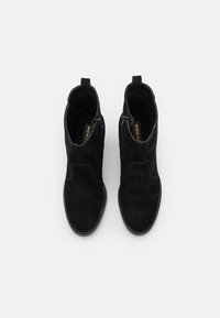 Ett par svarta mocka ankelstövlar med sidodragkedjor och dragflikar, visade uppifrån mot en vit bakgrund.