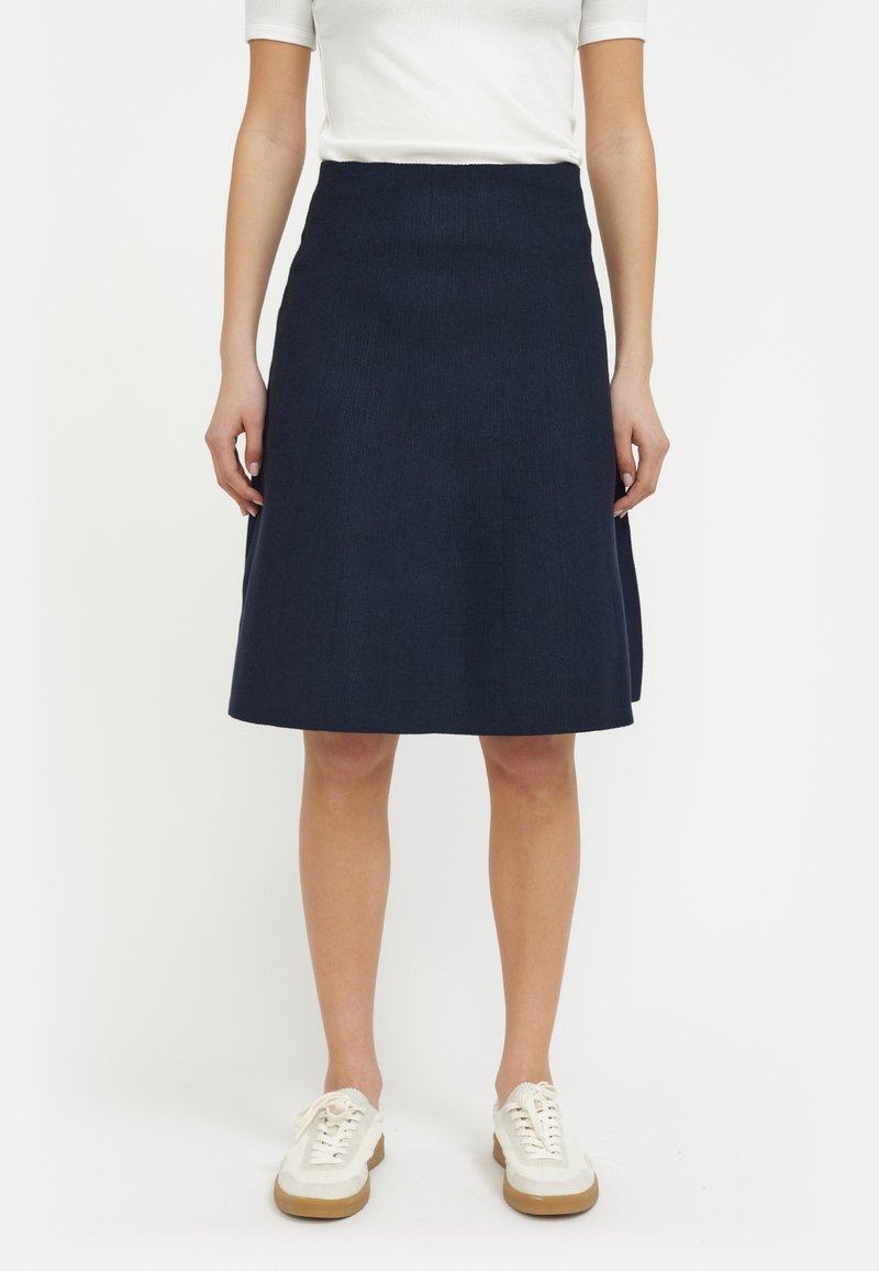 Jupe A-line bleu marine en tissu texturé, dotée d'une taille haute et d'un ourlet évasé. Associée à des baskets blanches.